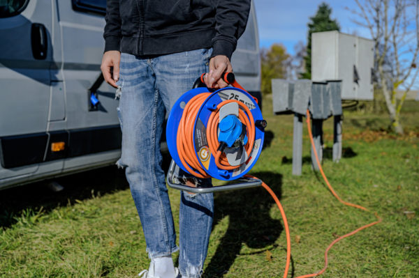 En person som står bredvid en husbil med en slang och Husvagns kabelvinda med 25m H07RN-F 3x2,5mm Orange fäst på.